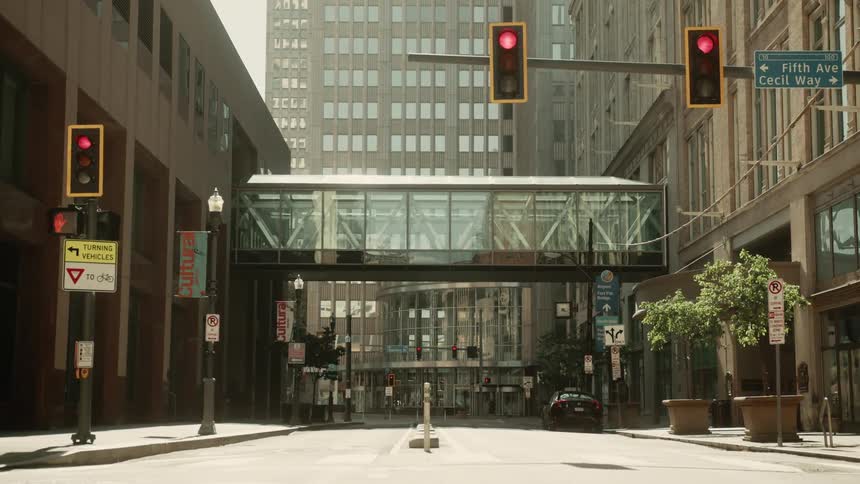 Traffic lights change from yellow to red near a walkway stretching between two buildings