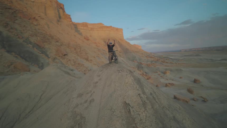 Person on bike with arms raised in triumph at the top of a narrow rock formation