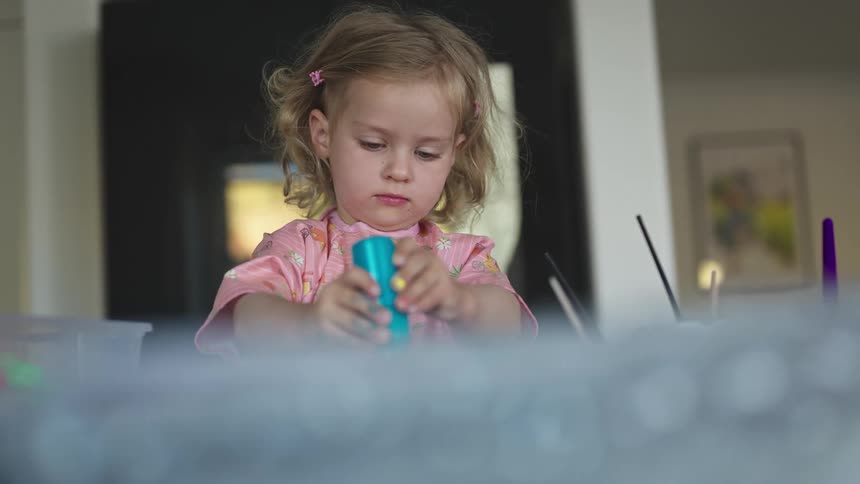 Young blonde girl squeezes blue paint from a bottle