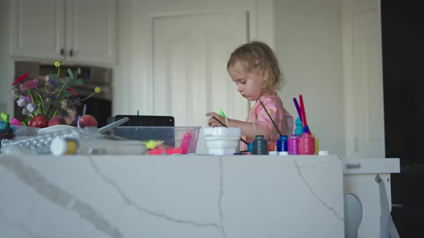 Small blonde girl playing with paint tubes