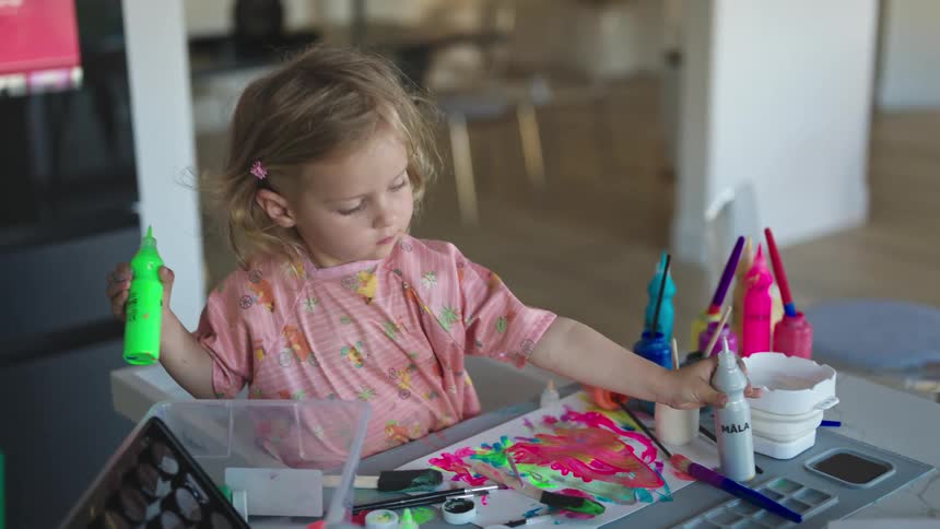 Young blonde girl fills palette with neon green paint while painting at home