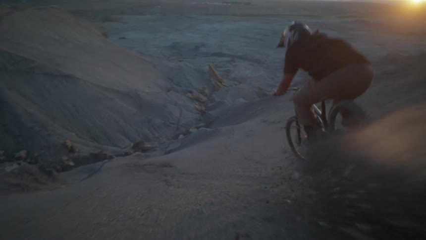 Man riding a mountain bike down the side of a mountain with a sunset on the horizon