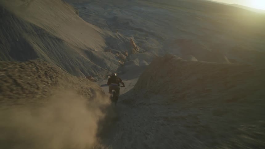 A person riding a bicycle down a narrow dirt trail between tall steep rock formations