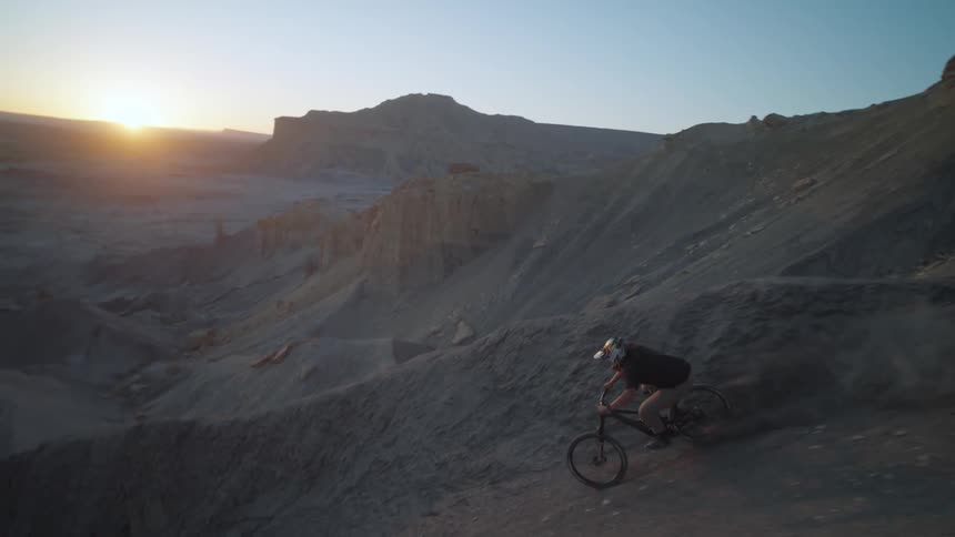 Cyclist rides bicycle down dirt slope in uneven terrain during sunset