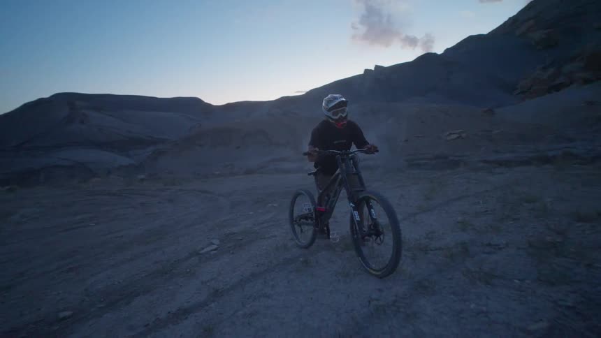 Person walking with his bike in mountainous terrain at sunset