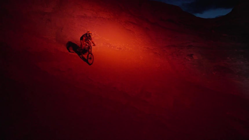 A cyclist riding on rugged terrain at dusk illuminated by a red light