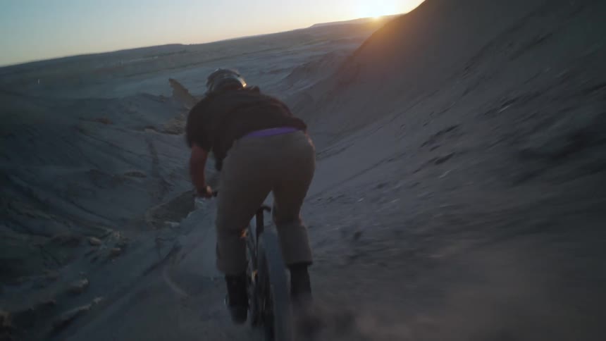 A man rides a bike through a desert landscape at dusk