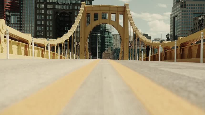 Yellow bridge with large arches leading to the center of a city with skyscrapers