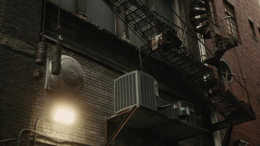 An air conditioner sits on a shelf near a buildings fire escape stairs