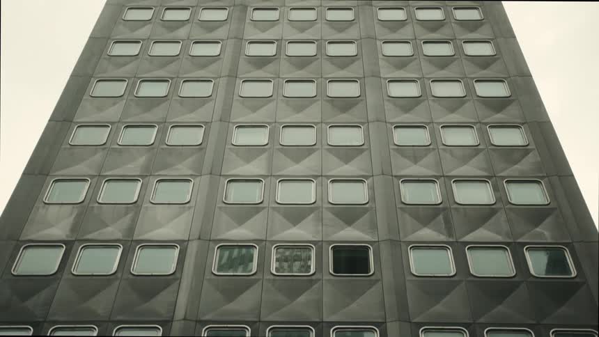A small gray building with several floors and several glass windows