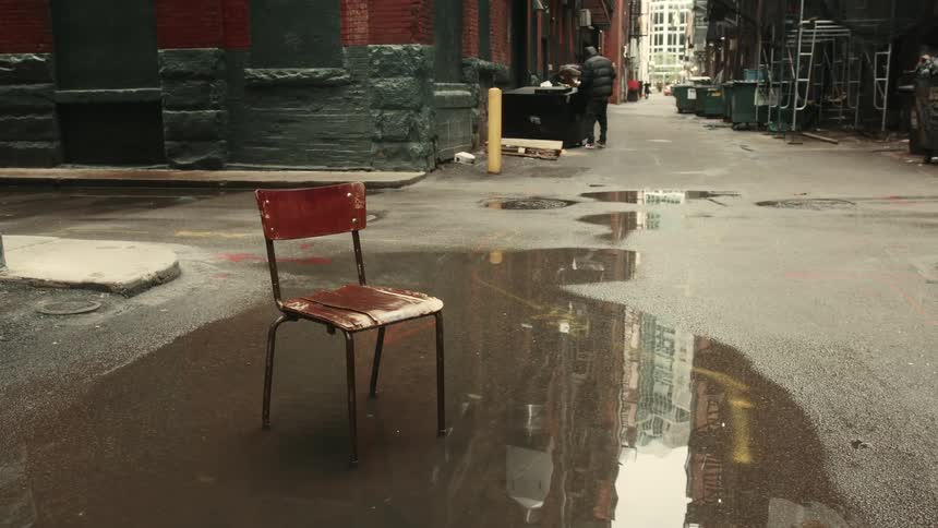 A wooden chair is in a puddle of water on an asphalt street