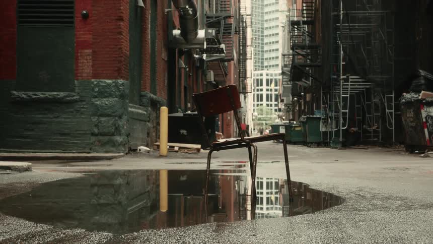 Broken chair stands in a puddle in an alley between downtown buildings