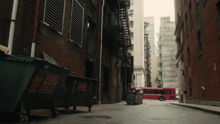 People walk by the entrance to a city alley as a bus passes by them