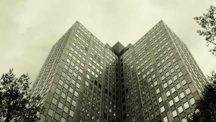 High rise building windows reflect another building under an overcast sky