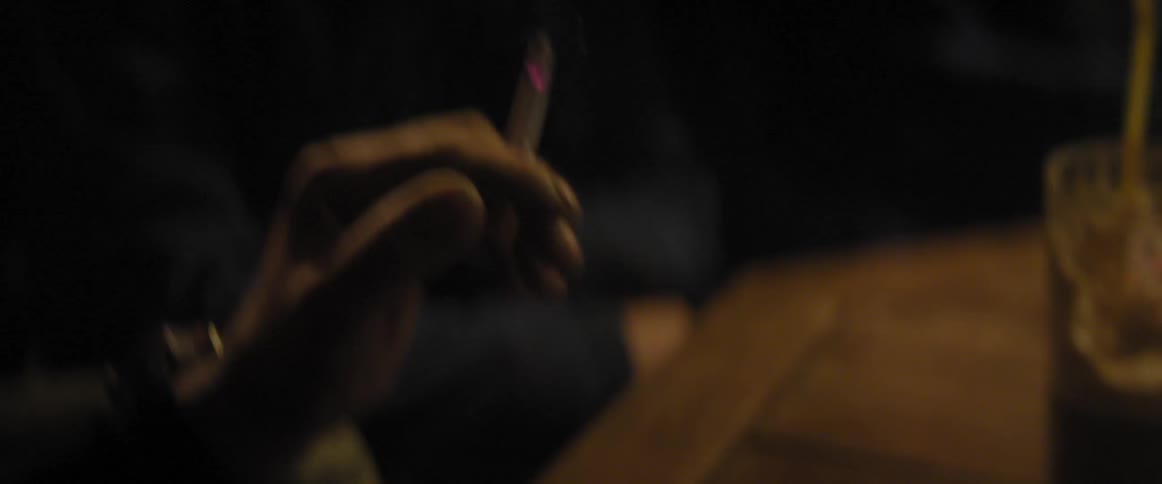 A man using his hands for emphasis, while holding a cigarette, as he speaks to other gathered around a table