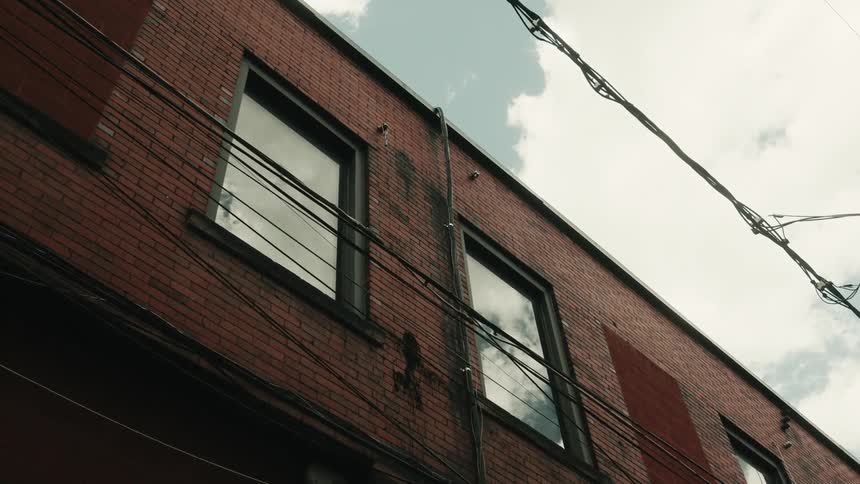 Upward view of the facade of a red brick building with windows and electrical wires against a cloudy sky