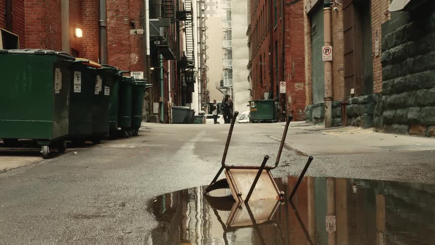 Old chair sits upside down in puddle in alley between buildings