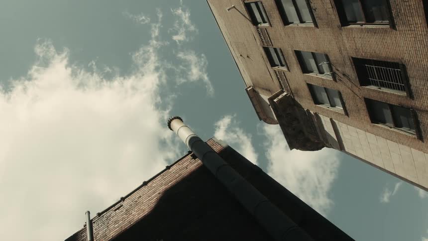 A tall smokestack stands between two brick buildings against a cloudy sky