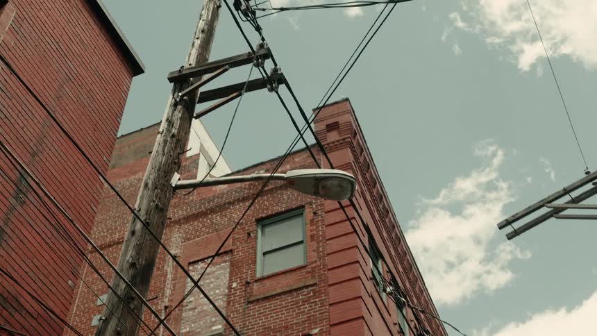 Utility pole with a streetlight stands next to mid rise building corner on a cloudy day