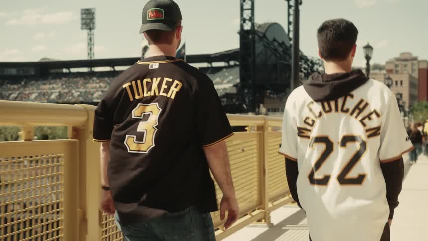 Two sports fans wearing jerseys walk towards a stadium