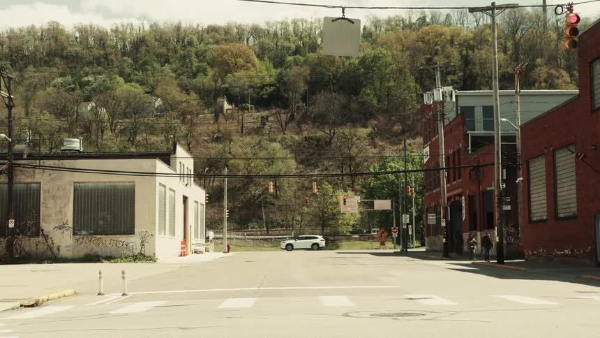 Vehicles cross intersections bordering warehouses and factories near a hill