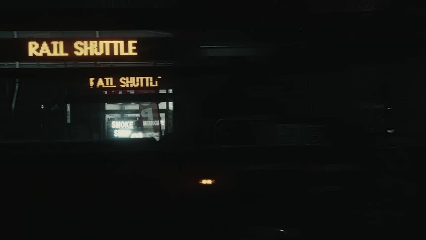 Bus stopping on a dark city street with a convenience store in the background