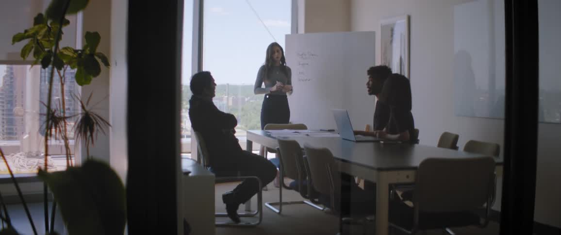 Woman holds meeting with coworkers in conference room overlooking downtown