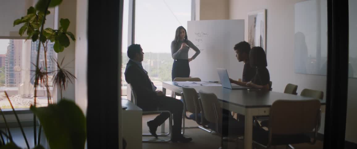 Woman standing and talking to three other people who are sitting at an office table