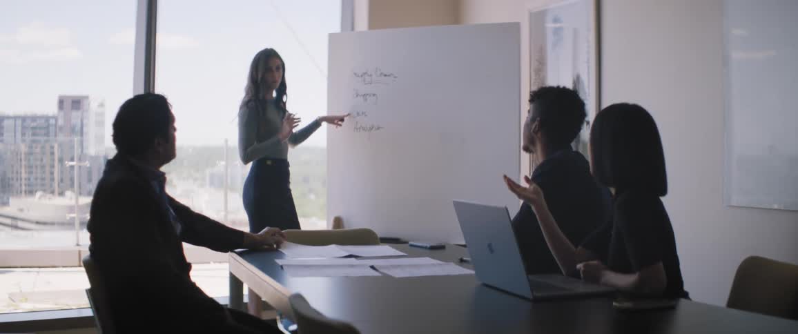 Four people in an office environment with one of them writing on a whiteboard