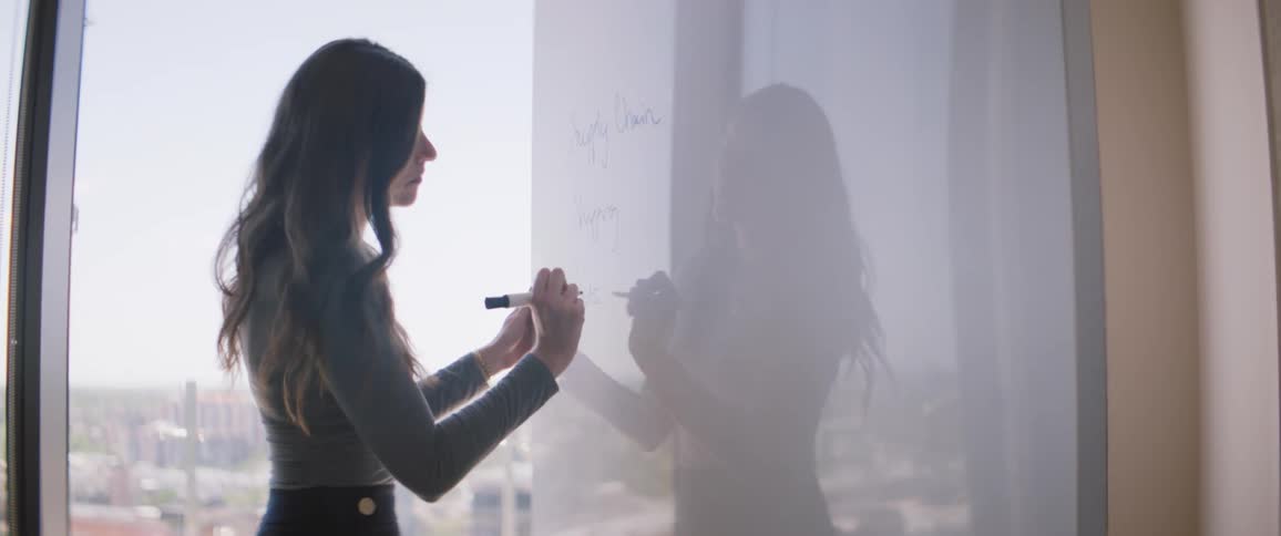 Woman stands near window writing on whiteboard