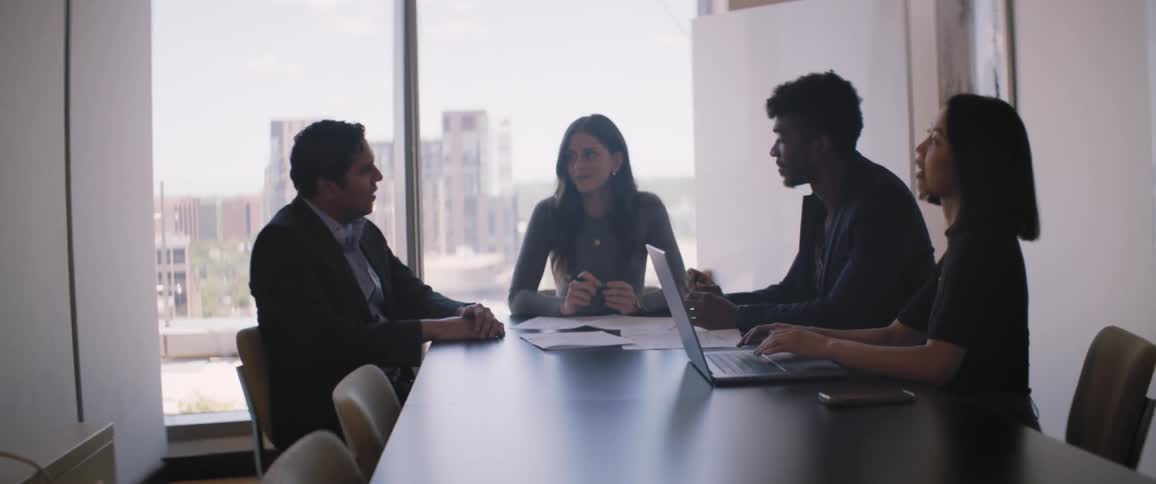 Four people sitting at an office table in a meeting talking