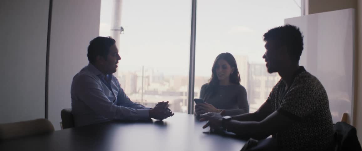 Groups of three people sitting at an office table talking