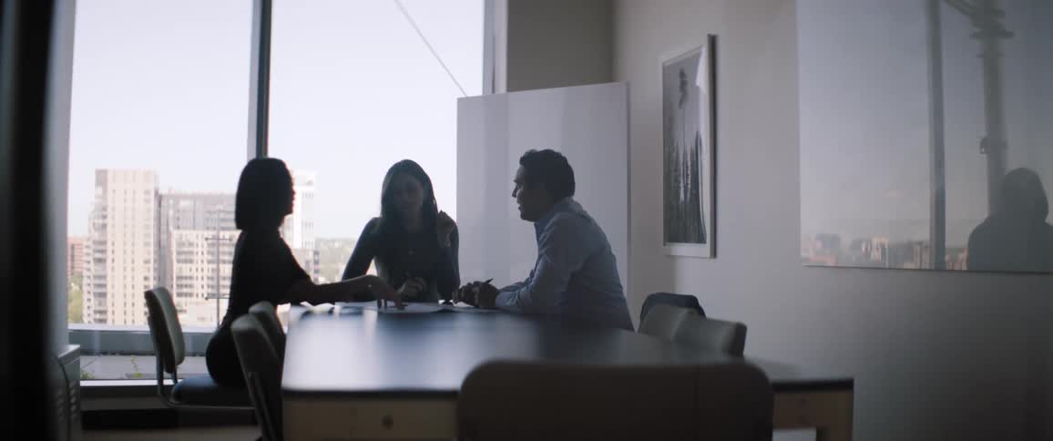Three people sit at a table in an office and have a conversation