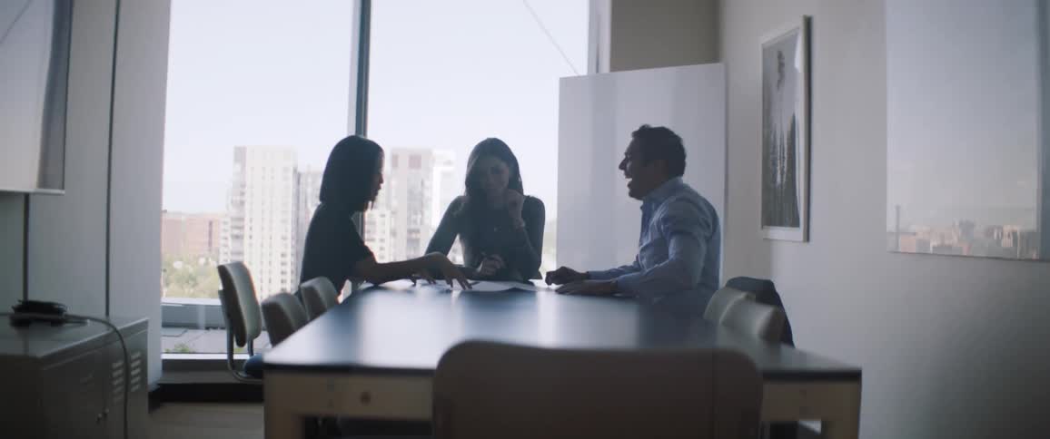 Three people in an office sitting at a table talking in a meeting