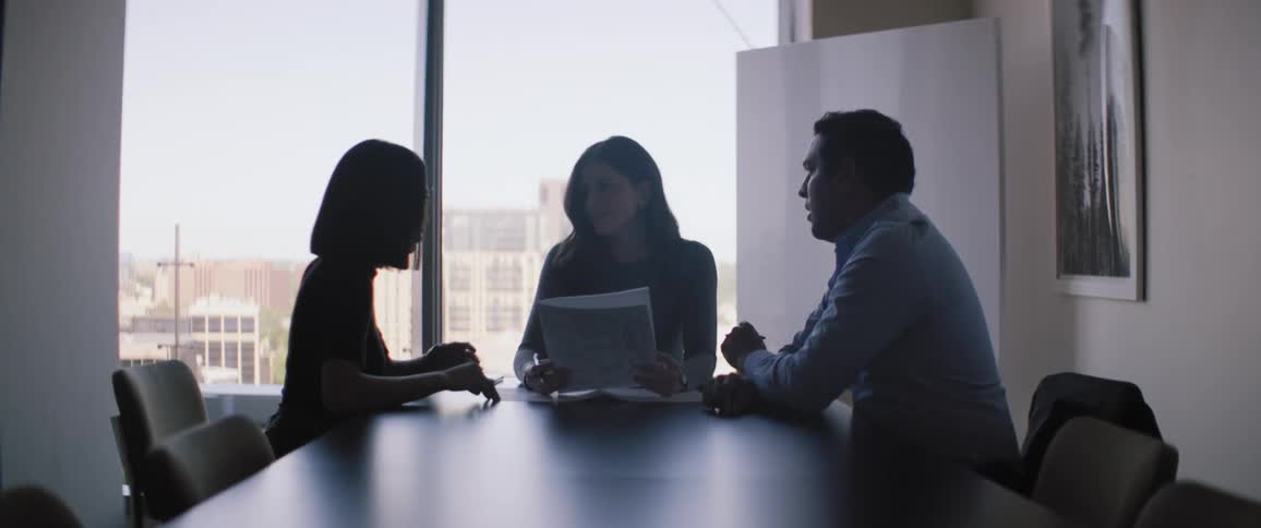 A black table with two women and a man and they are talking and one of the women is holding a paper