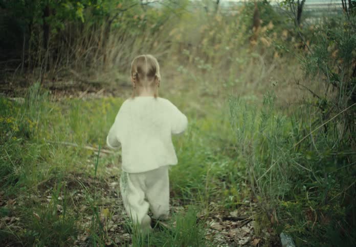 Little blonde girl walking through the woods in an outdoor environment