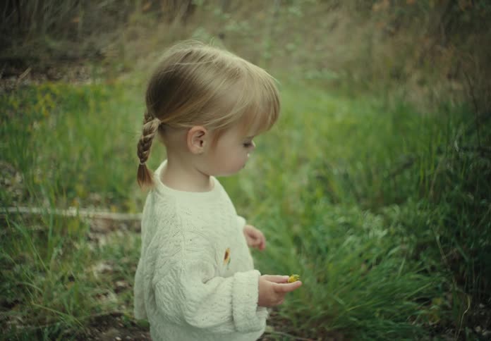 A small child stands on a grassy area as another person turns away and walks off