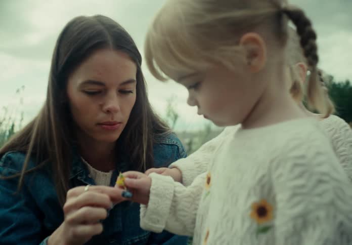 A mother hands a flower to one of her two daughters outdoors