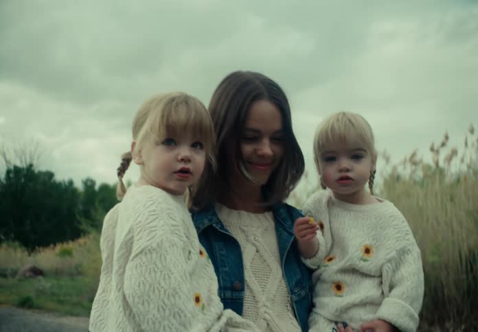 A mother and her daughters walk down a gravel path next to a field