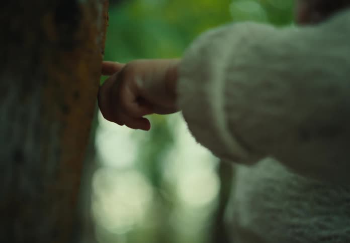 A human hand with its finger touching a tree trunk and the person is wearing a white coat with long sleeves