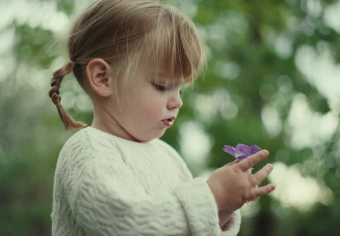 A little blonde girl in white clothes holding a violet flower