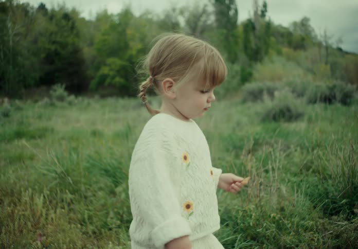 Little blonde girl walking in a greenish field