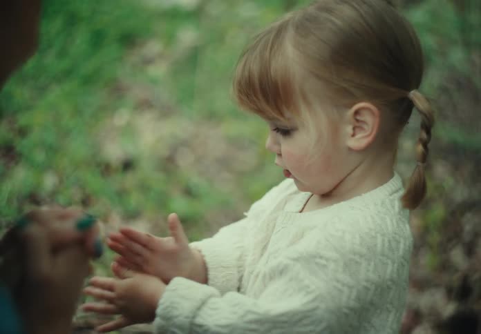 A mother and daughter enjoy clapping their hands on a grassy field