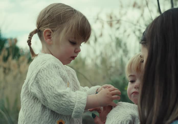 Two little twin girls with their mother in a field on a cloudy day