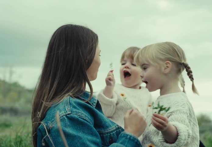 Mother holding her two twin daughters on her lap playing with plants