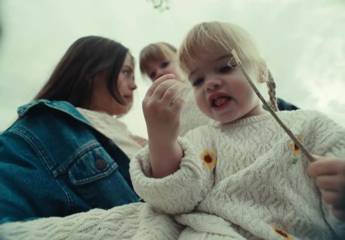 Mother sitting in a field with her two young daughters with one of them holding a small wooden branch
