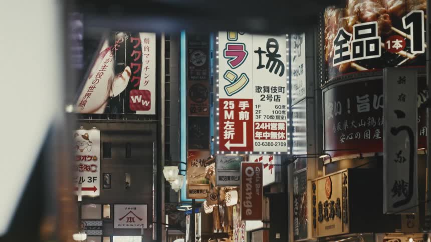 Dolly shot of buildings and Japanese billboards and advertisements light up the night in Tokyo Shinjuku