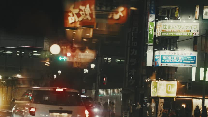 A nighttime street scene with illuminated signs traffic lights and cars