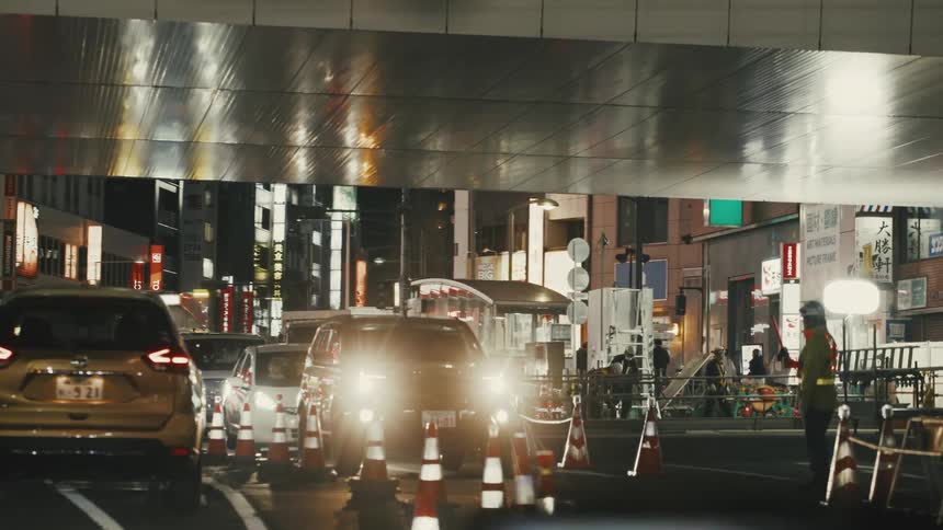 Night urban scene with vehicles and artificial lighting highlighting traffic cones lined up on the street and stores with bright signs in the background