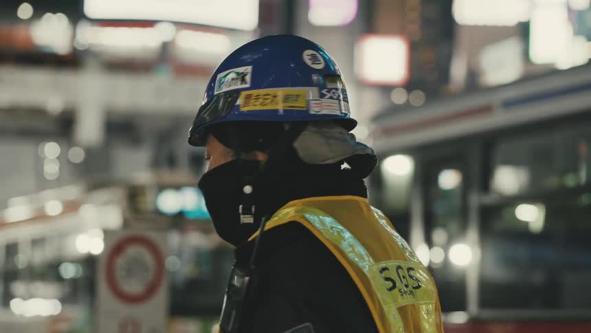 Woman with helmet and safety clothing looking sideways in a metropolis with buses or background passing by at night